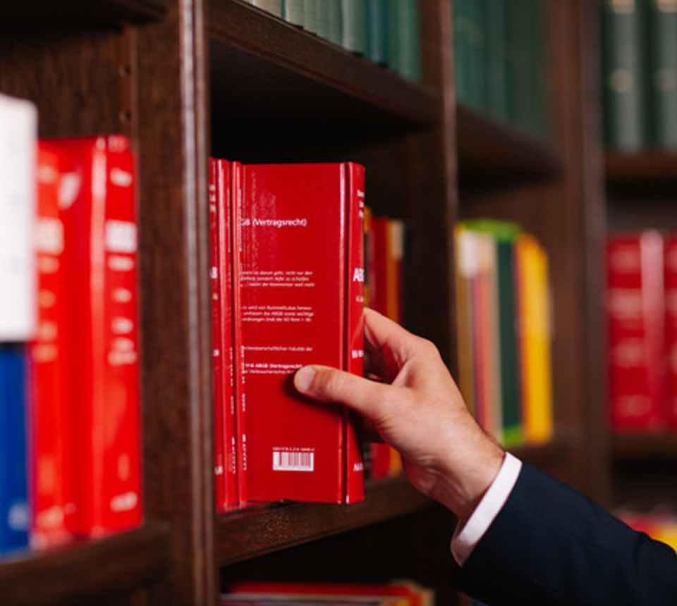 Detailaufnahme der Hand einer Person, die ein Gesetzbuch aus dem Regal nimmt